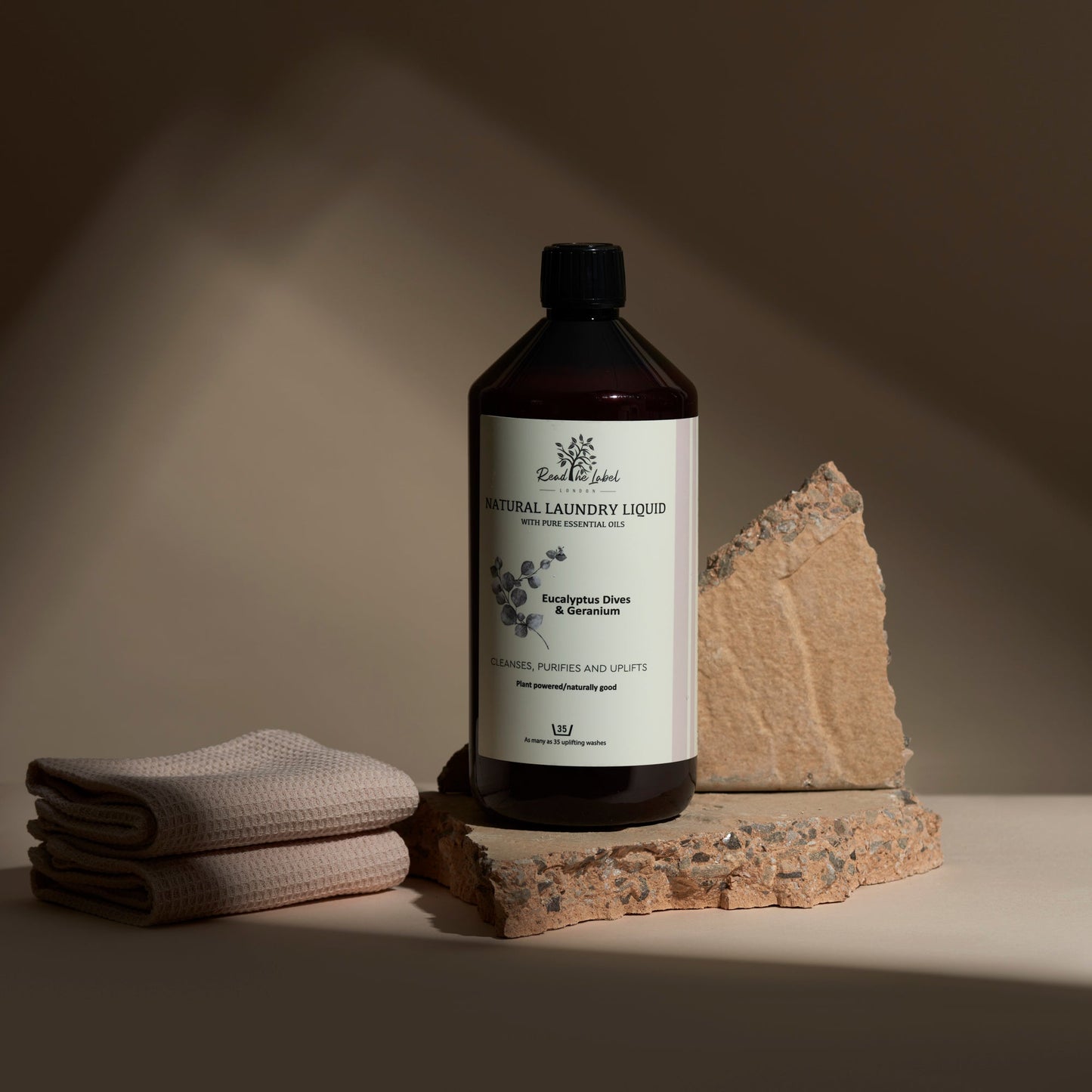 Bottle of natural laundry liquid with a label, folded towel, and stone on a neutral background