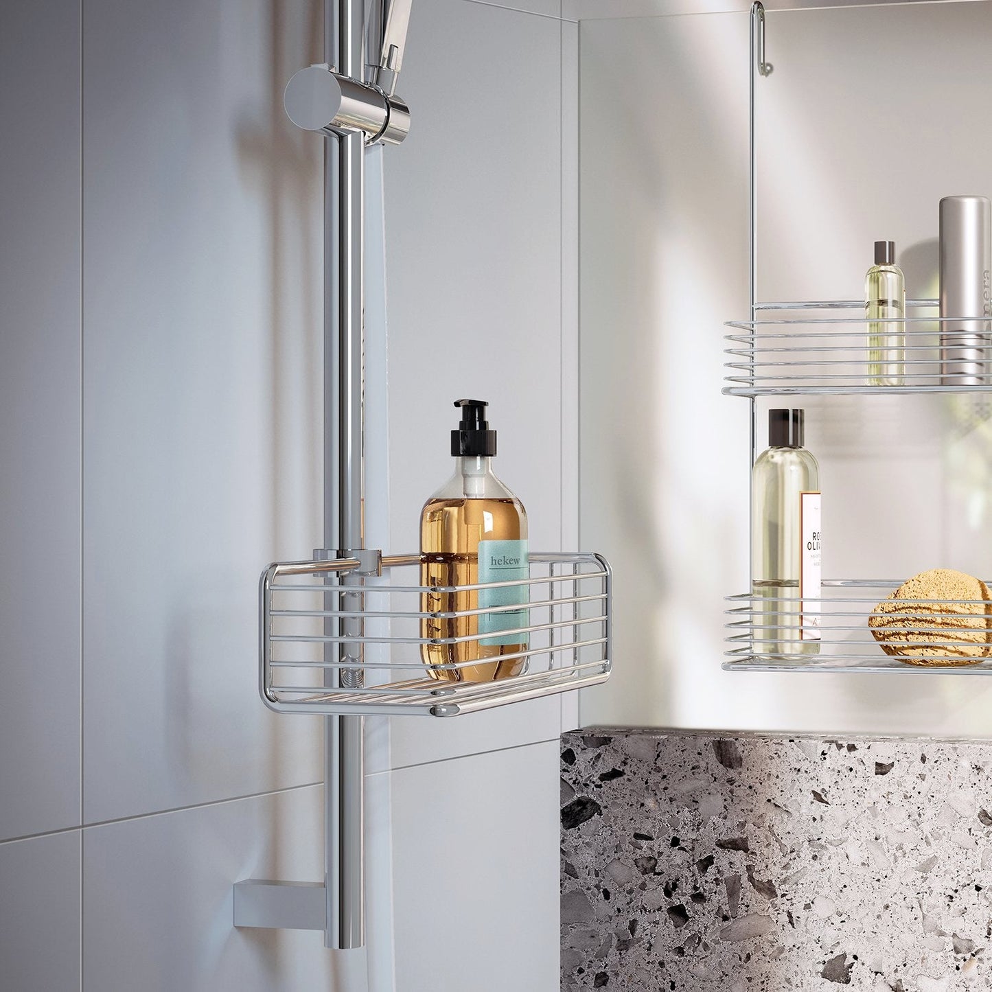 Smedbo Sideline DK1106 Chrome Riser Rail Basket in Use — Holding Amber Pump Bottle on Chrome Shower Rail, Mirror Reflection Showing Second Basket with Shower Oils and Natural Sponge, Terrazzo Bath Surround