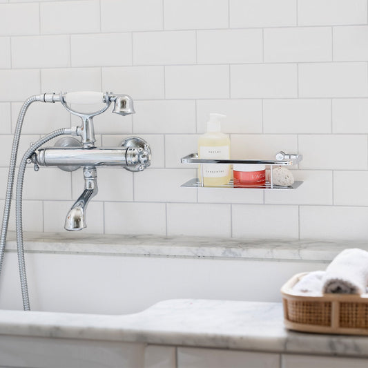 Smedbo Sideline DK3001 Polished Chrome Shower Basket with Solid Tray — Wall-Mounted on White Subway Tiles Above Marble Bath, Styled with Skincare Products