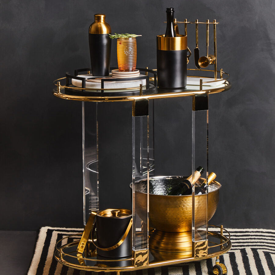 Two-tiered bar cart with gold and black decor against a dark background