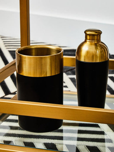 Two black and gold cylindrical containers on a glass table with a geometric pattern.
