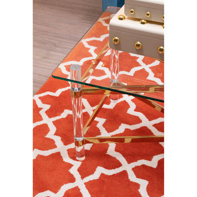 Glass coffee table with gold legs on a red and white patterned rug