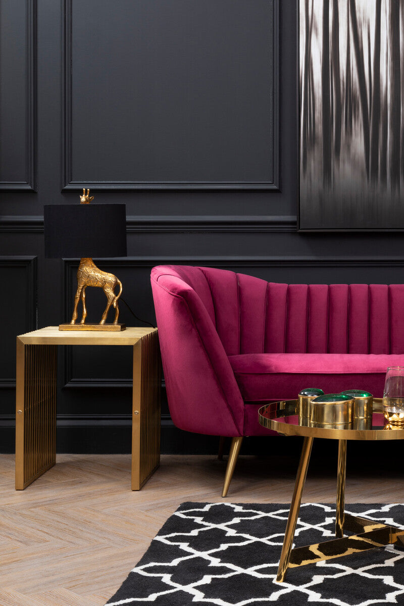 Pink velvet sofa in a room with black walls, gold side table, and decorative lamp.