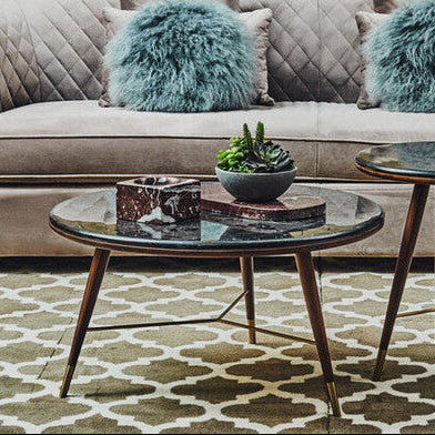Round glass coffee table with decorative items on a patterned rug in a living room setting.