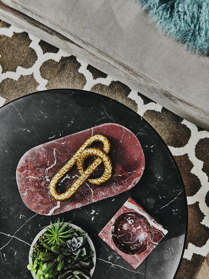Decorative stone with gold chain on a black marble surface, surrounded by small plants.
