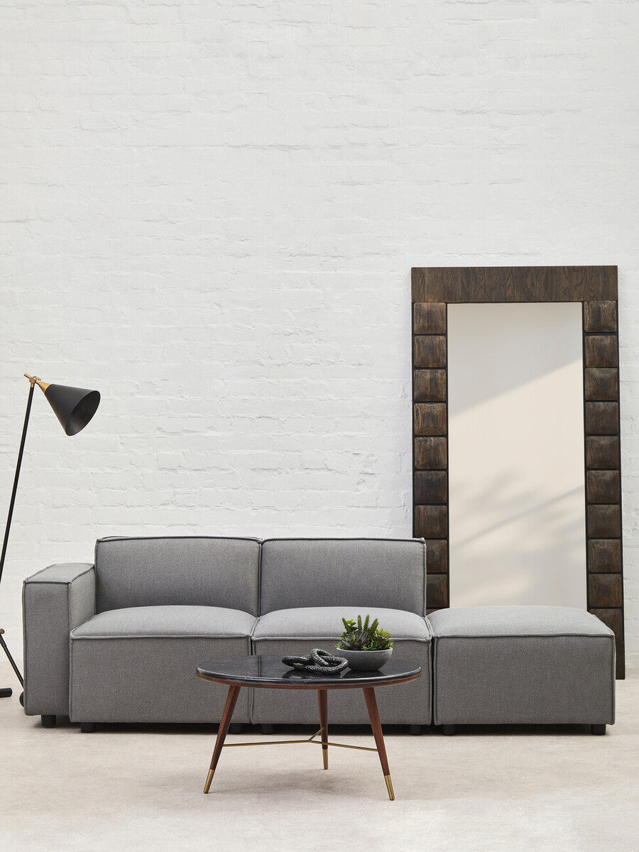 Gray sectional sofa with a coffee table in a room with a white brick wall and a tall mirror.