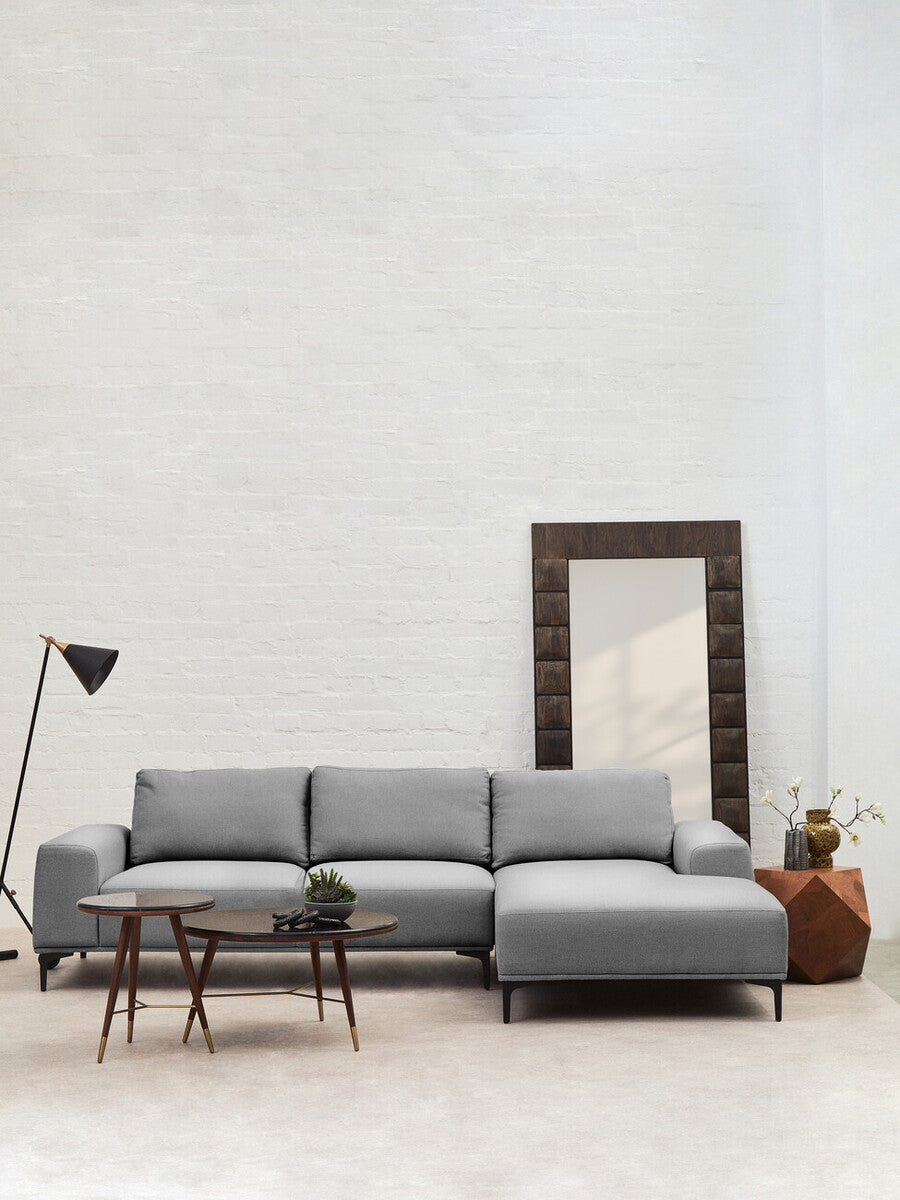 Gray sectional sofa in a minimalistic room with a mirror and small tables.