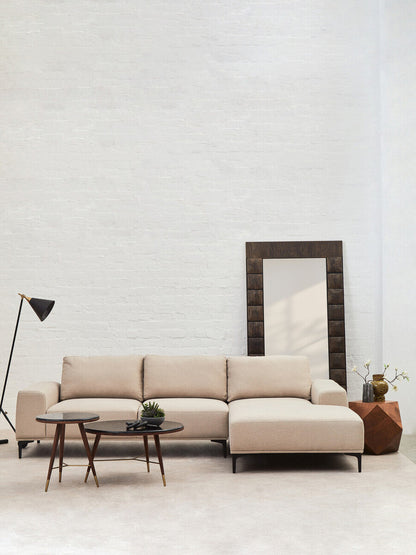 Beige sectional sofa in a minimalistic living room with a mirror and side tables.