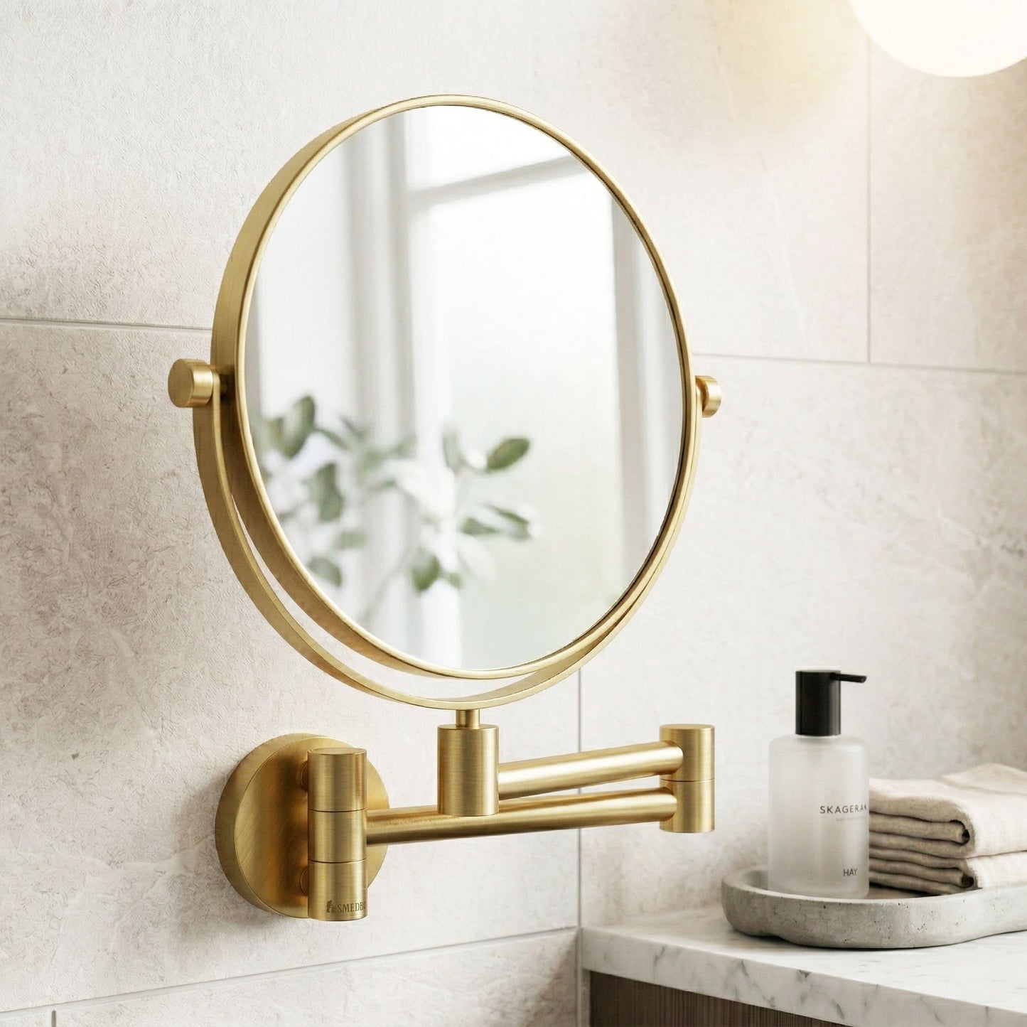 Gold wall-mounted mirror in a bathroom setting with a white tiled wall and a small table with a bottle and towels.