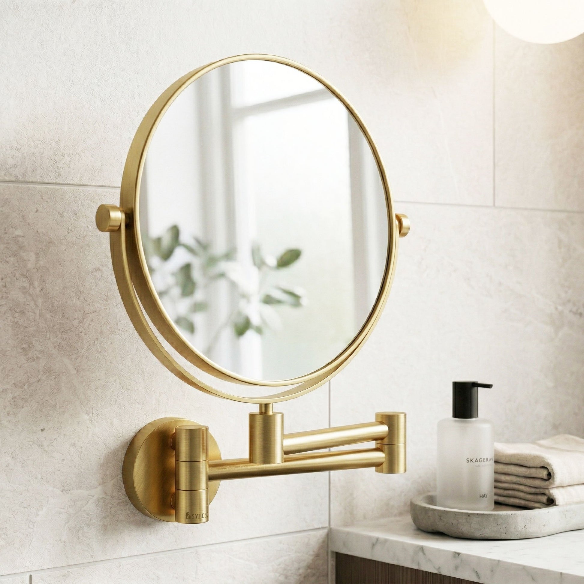 Gold wall-mounted mirror in a bathroom setting with a white tiled wall and a small table with a bottle and towels.