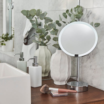 Makeup mirror and soap dispenser on a bathroom counter with toiletries and decor