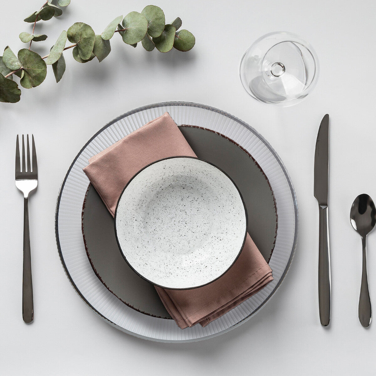 White glass charger plate laid beneath a dinner plate in a place setting
