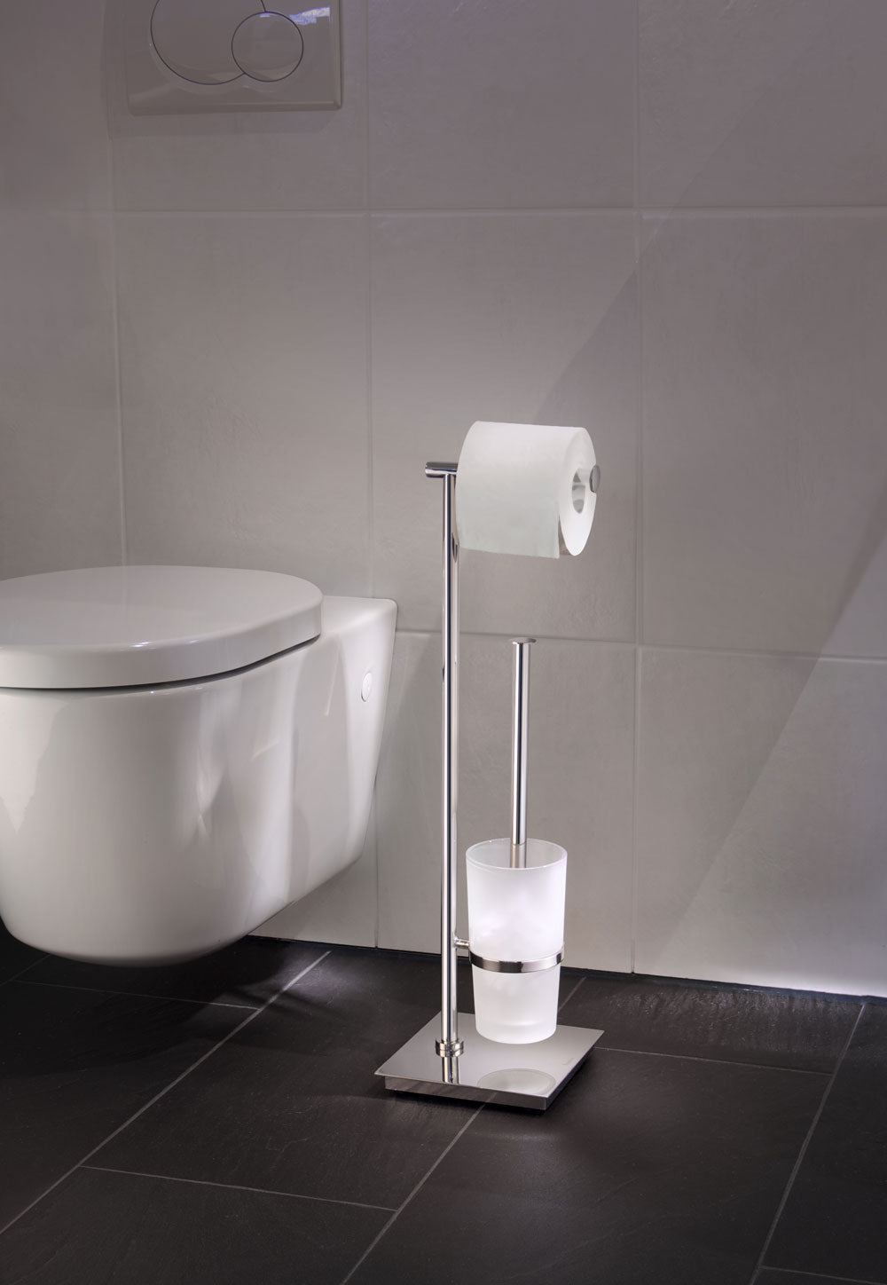 Smedbo Outline Lite FK603 Polished Steel Toilet Butler in Use — Square Base on Dark Slate Floor Tiles Beside Wall-Hung Toilet, Toilet Roll Loaded and Frosted Glass Brush Container Visible