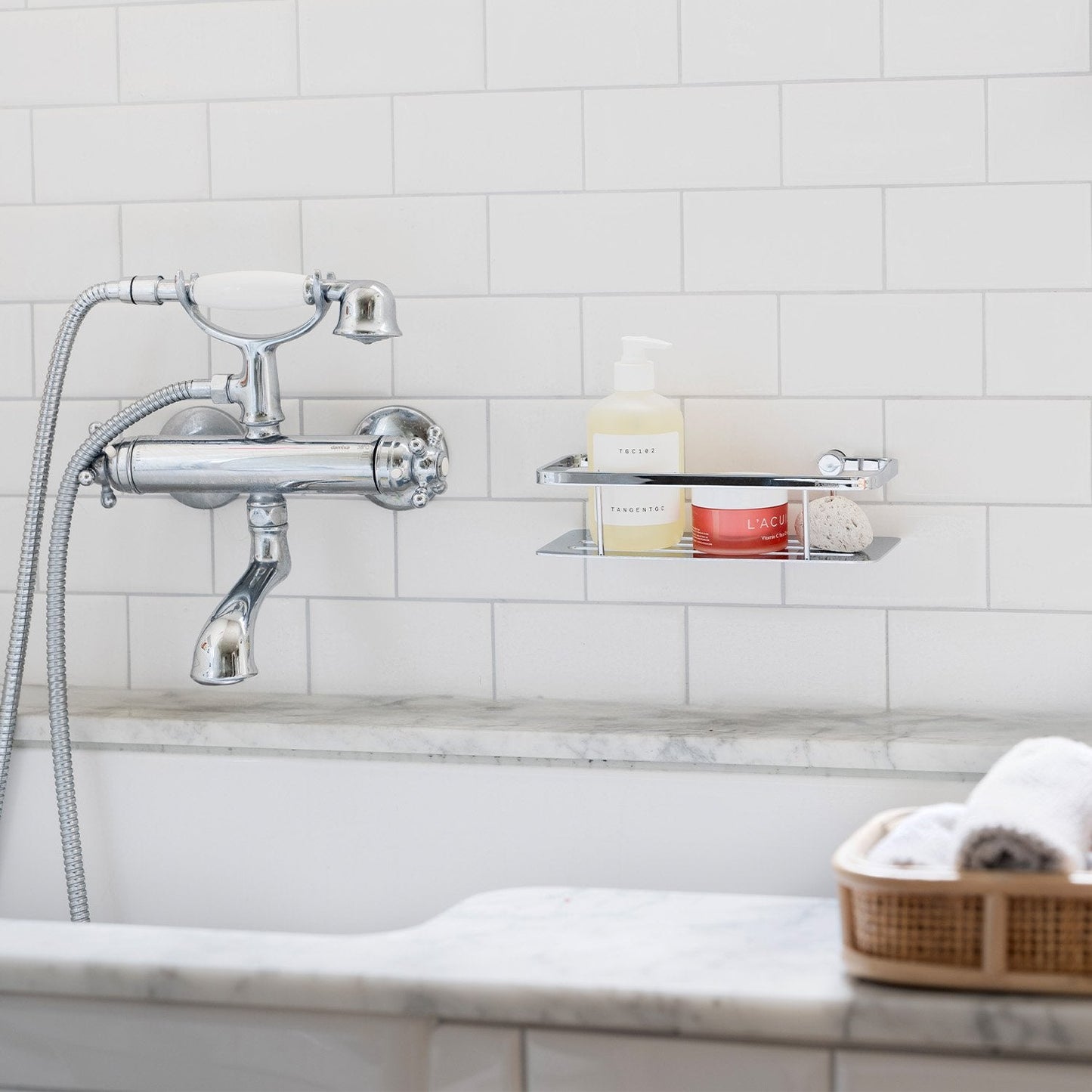 Smedbo Sideline DK3001 Polished Chrome Shower Basket with Solid Tray — Wall-Mounted on White Subway Tiles Above Marble Bath, Styled with Skincare Products