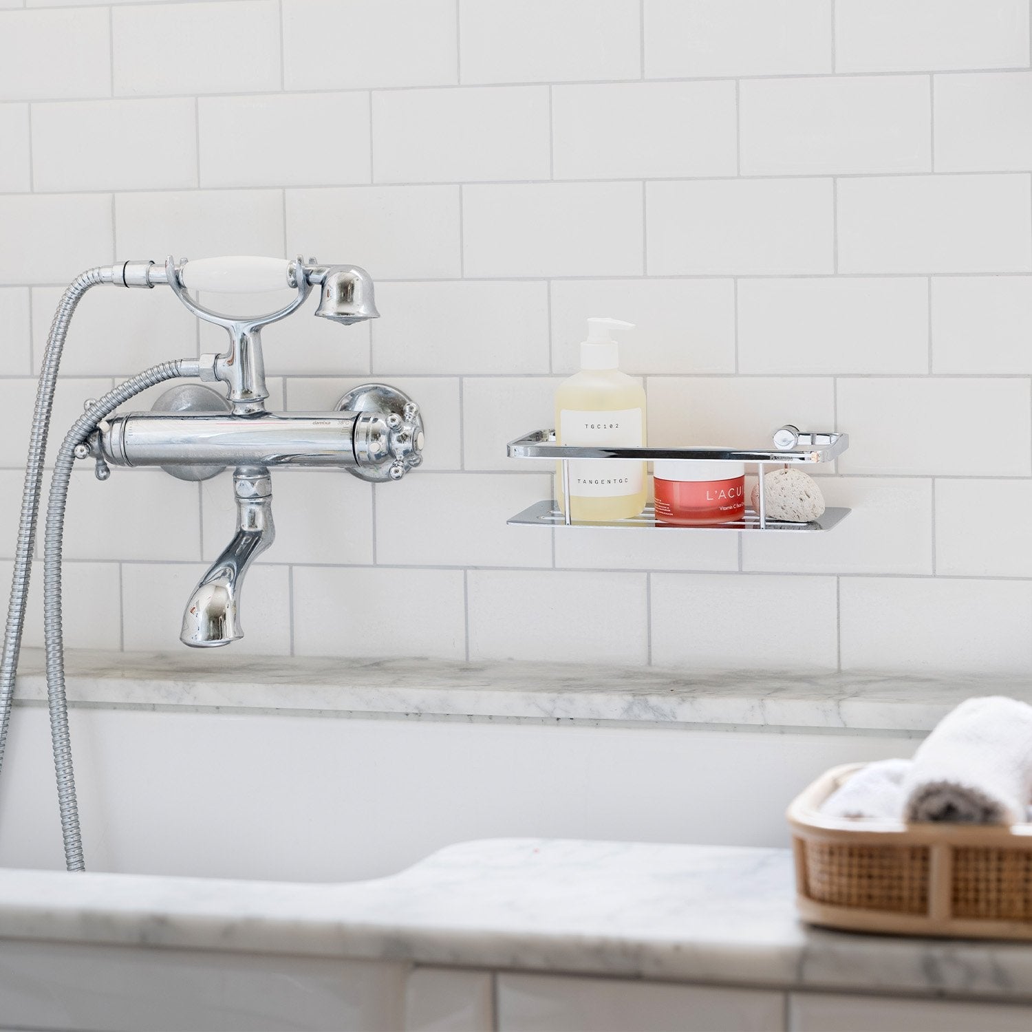 Smedbo Sideline DK3001 Polished Chrome Shower Basket with Solid Tray — Wall-Mounted on White Subway Tiles Above Marble Bath, Styled with Skincare Products
