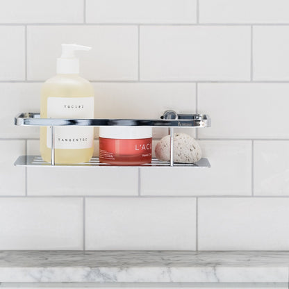 Smedbo Sideline DK3001 Polished Chrome Shower Basket — Close-Up of Solid Perforated Tray Styled with Pump Bottle, Skincare Jar and Pumice Stone on White Subway Tiles