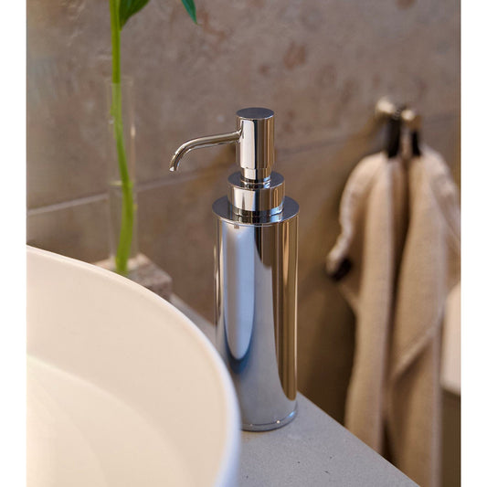 Smedbo Outline FK254 Polished Chrome Freestanding Soap Dispenser on White Stone Vanity Beside Round Countertop Basin — Bamboo Stem and Linen Towel in Background