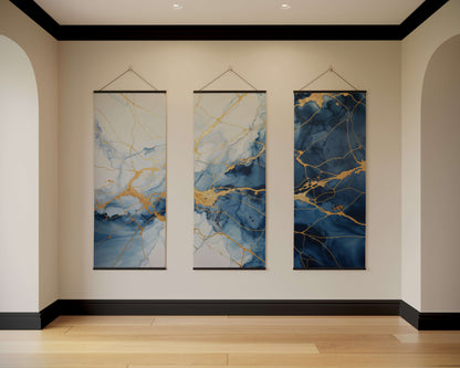 Three abstract wall hangings with blue and gold patterns on a beige wall.