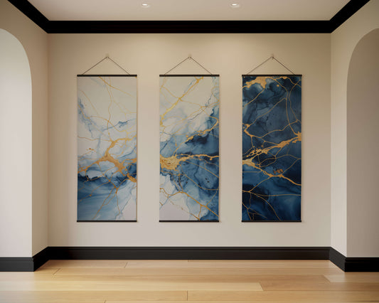 Three abstract wall hangings with blue and gold patterns on a beige wall.