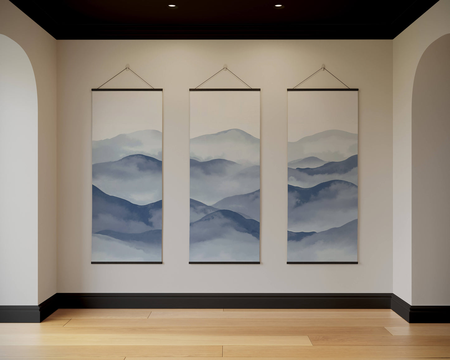 Three hanging wall art pieces depicting mountain landscapes in a room with beige walls and wooden flooring.