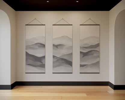 Three hanging landscape paintings on a wall in a room with wooden flooring.