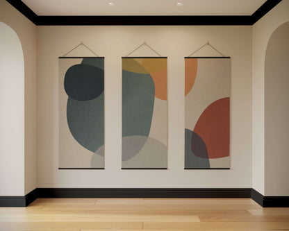 Three abstract wall hangings on a beige wall with wooden flooring.