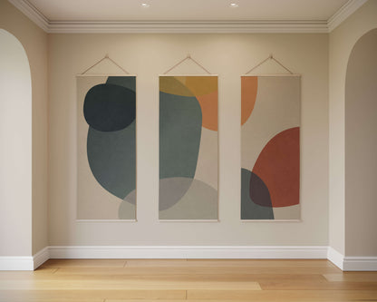 Three abstract wall hangings on a beige wall with wooden flooring.