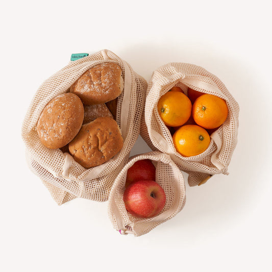 3 Wild and Stone Organic Cotton Mesh Produce Bags filled with bread rolls, oranges and apples on a white background