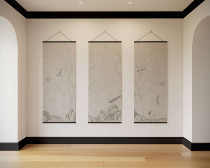 Three hanging scrolls on a wall in a room with wooden flooring and black baseboards.