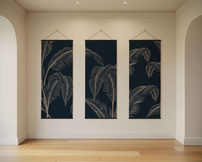Three vertical wall art pieces with leaf patterns hanging on a beige wall.