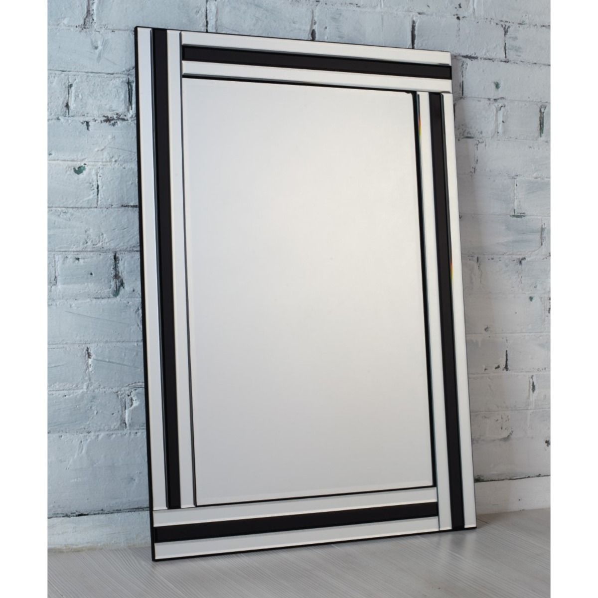 Large mirror with black frame leaning against a light grey brick wall.