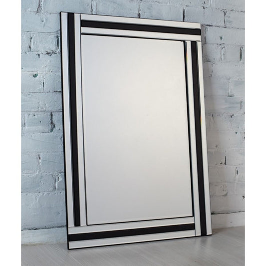 Large mirror with black frame leaning against a light grey brick wall.