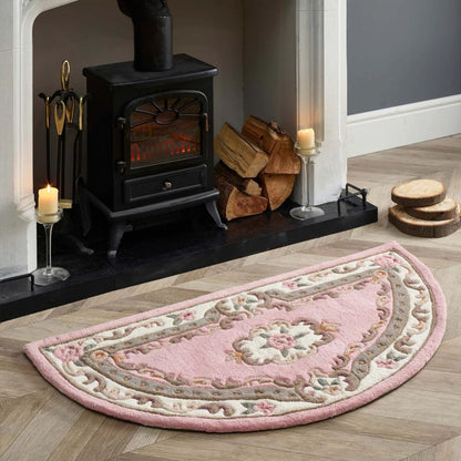 Decorative pink rug on a wooden floor with a fireplace and candles in the background.