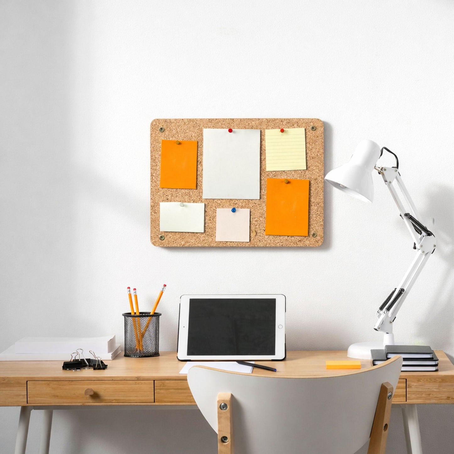 Cork bulletin board with sticky notes on a wall above a desk with office supplies.