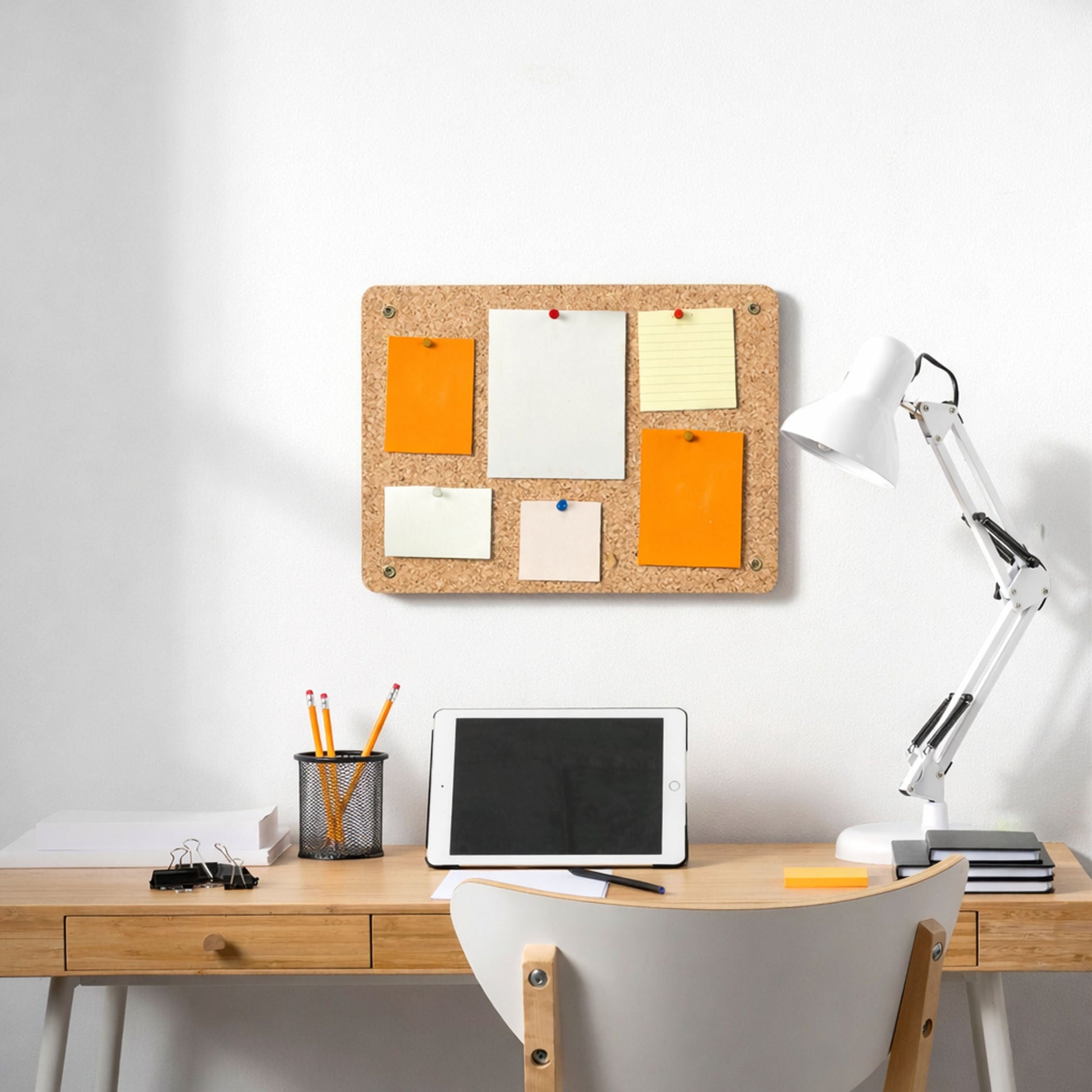 Cork bulletin board with sticky notes on a wall above a desk with office supplies.