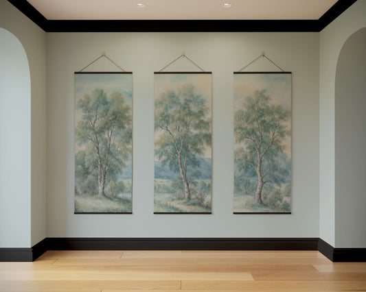 Three tree paintings hanging on a wall in a room with wooden flooring.