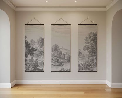 Three landscape paintings hanging on a wall in a room with wooden flooring.